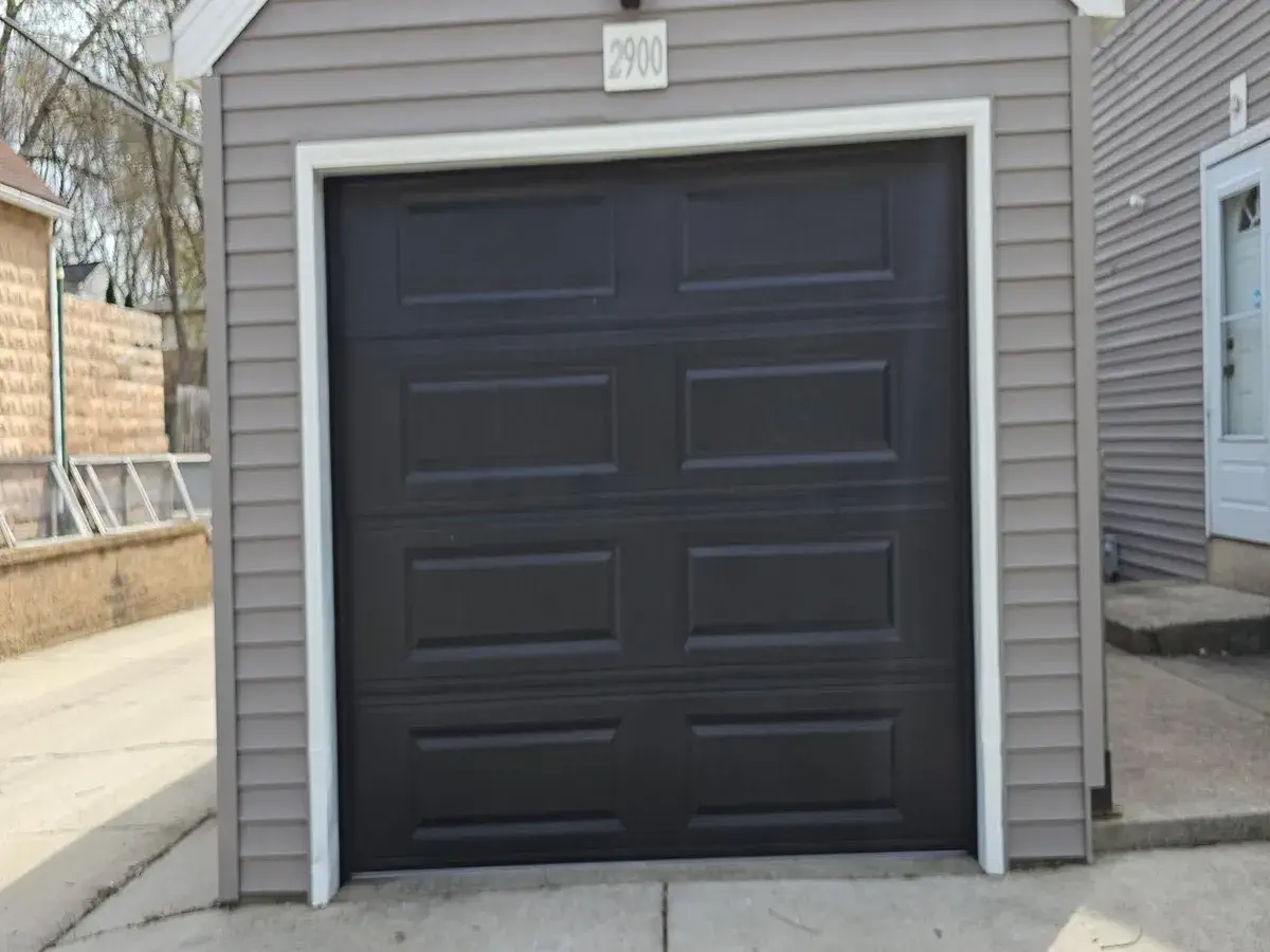 Black single garage door installed on a gray sided garage