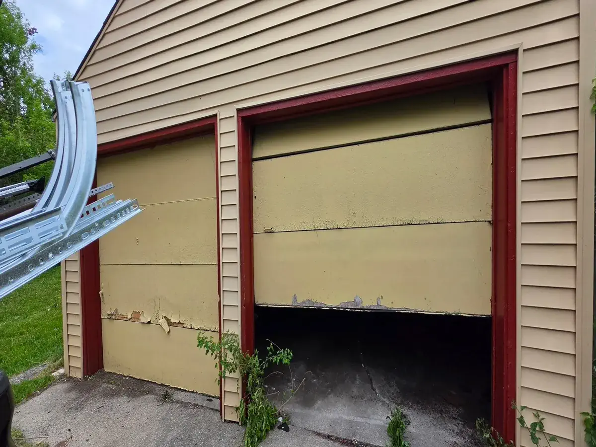 Collapsed garage door on a tan sided garage before replacement