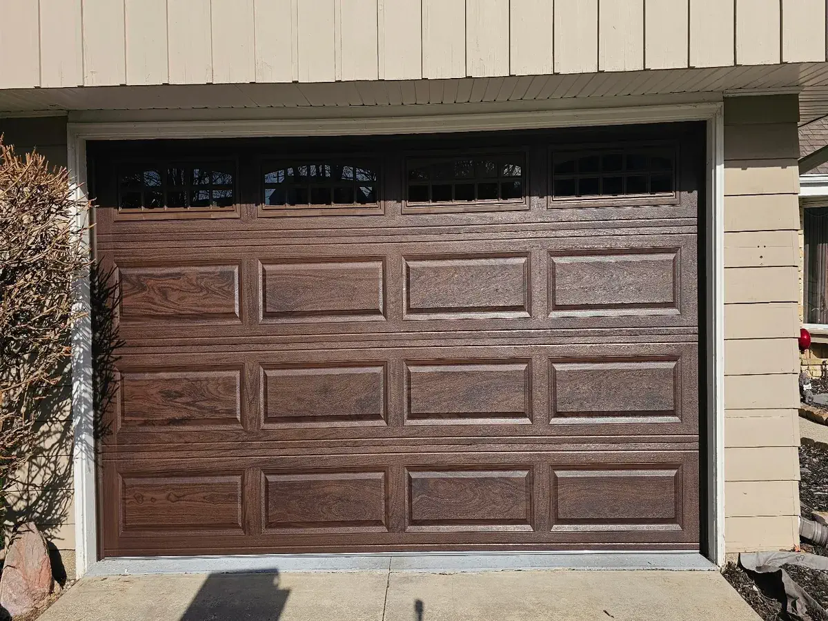 Dark brown woodgrain garage door with a row of windows on a tan sided garage