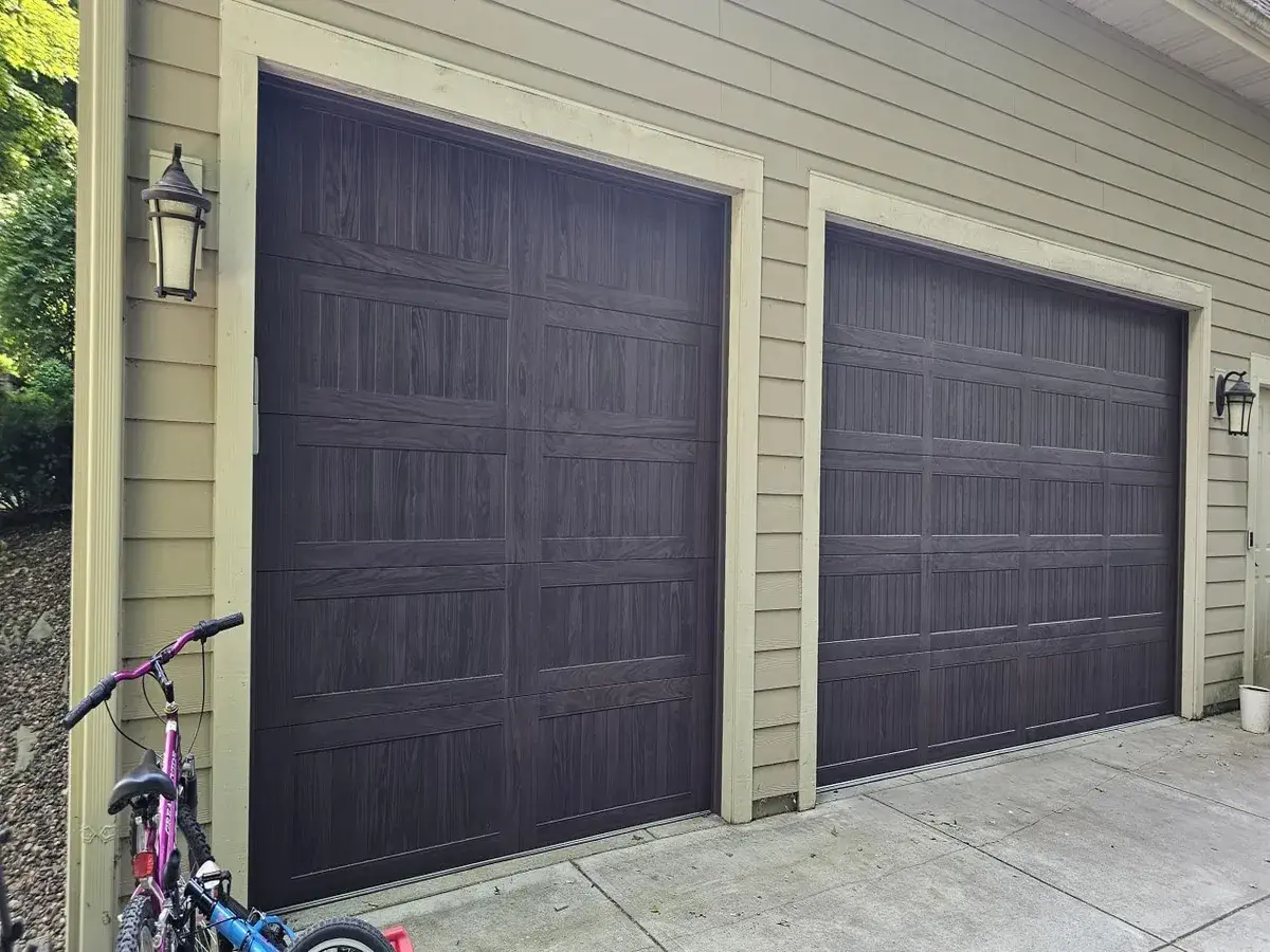Two dark brown woodgrain garage doors on a cream sided garage