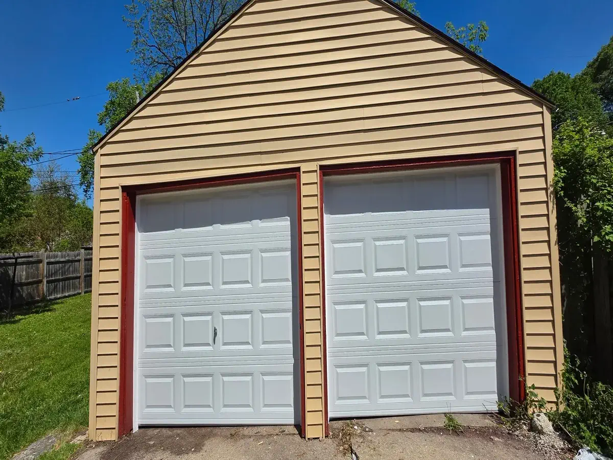 Two white single garage doors installed on a tan sided garage with red trim